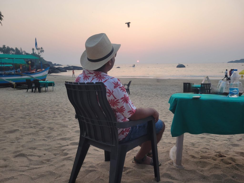 Beautiful view of Palolem Beach in Goa, India, showcasing a serene sandy shoreline lined with lush palm trees and colorful beach huts. The calm blue waters and clear sky create a picturesque and tranquil atmosphere, perfect for a relaxing beach getaway.